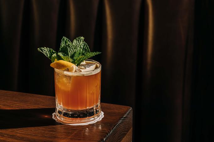 Product: A glass of iced cocktail garnished with mint leaves and a lemon slice, placed on a wooden surface against a dark background. - Gus' Sip and Dip in Chicago, IL Restaurants/Food & Dining