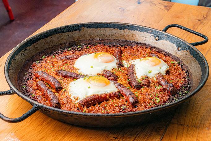 Product: A red rice dish with pieces of sausage and fried eggs, in a cast iron pan on a wooden table - Cafe Ba-Ba-Reeba! in Lincoln Park - Chicago, IL Gluten Free Restaurants