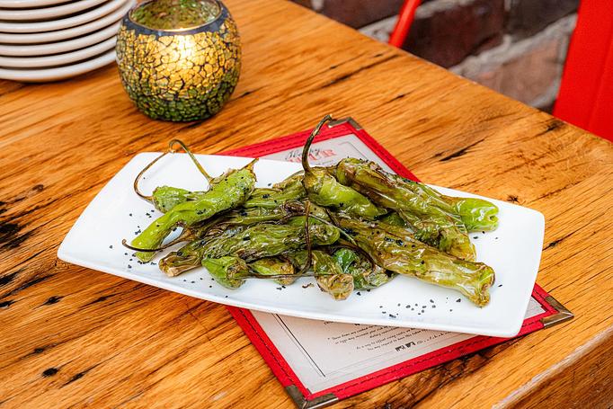 Product: A pile of green peppers on a long, white, rectangular dish, sprinkled with spices and herbs, sitting on a Cafe Ba-Ba-Reeba menu on a wooden table - Cafe Ba-Ba-Reeba! in Lincoln Park - Chicago, IL Gluten Free Restaurants