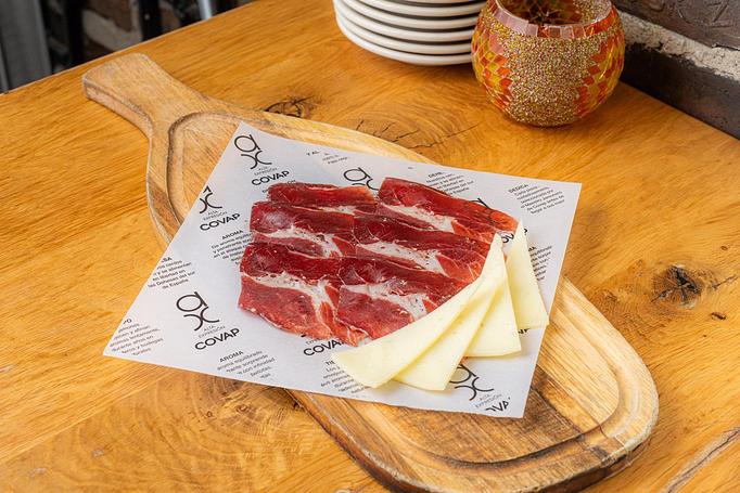 Product: Thin red slices of ham, striped with white fat, served with triangles of white cheese, on a piece of white paper with words on top of a wooden board - Cafe Ba-Ba-Reeba! in Lincoln Park - Chicago, IL Gluten Free Restaurants
