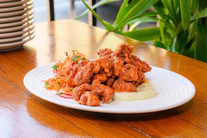 Product: Brown pieces of fried chicken garnished with green herbs, with a dollop of white sauce on a white plate, on a wooden table with green plants in the background - Cafe Ba-Ba-Reeba! in Lincoln Park - Chicago, IL Gluten Free Restaurants