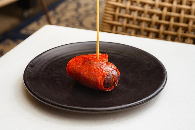 Product: A piece of pink chorizo wrapped around brown date speared with a toothpick, on a black plate - Cafe Ba-Ba-Reeba! in Lincoln Park - Chicago, IL Gluten Free Restaurants
