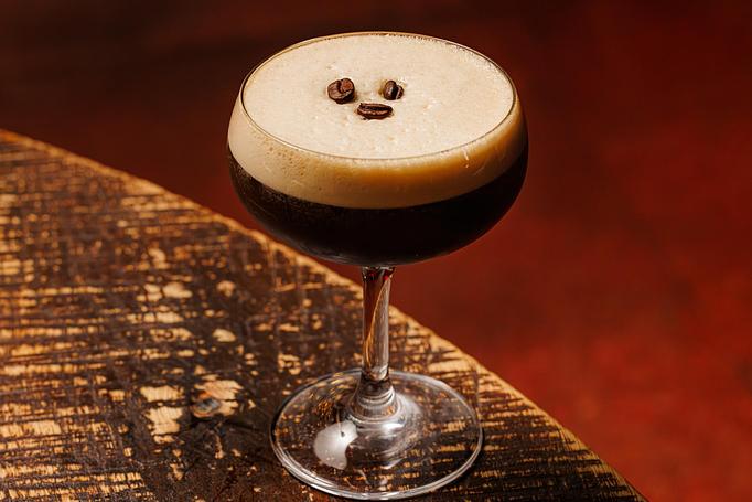 Product: A brown cocktail in a coupe glass with white foam on top, garnished with three coffee beans, on a wooden table - Cafe Ba-Ba-Reeba! in Lincoln Park - Chicago, IL Gluten Free Restaurants