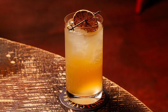 Product: An orange cocktail in a tall Collins glass with ice, garnished with a candied orange slice, on a Cafe Ba-Ba-Reeba! coaster on a wooden table. - Cafe Ba-Ba-Reeba! in Lincoln Park - Chicago, IL Gluten Free Restaurants