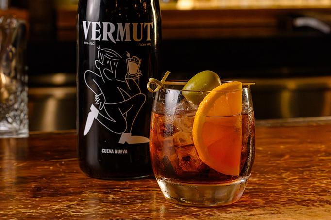 Product: Brown cocktail over ice in a short glass, garnished with an olive and an orange slice, sitting on a wooden table in front of a dark bottle of Vermut - Cafe Ba-Ba-Reeba! in Lincoln Park - Chicago, IL Gluten Free Restaurants