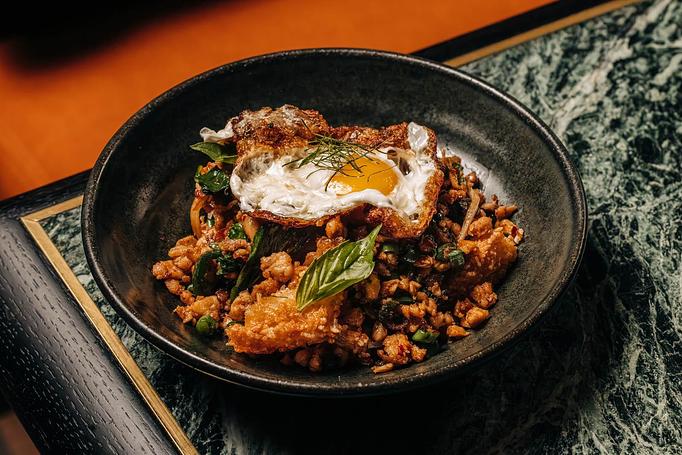 Product: A black bowl filled with a savory dish, including crispy rice, green herbs, and vegetables, topped with a fried egg. - Crying Tiger in Chicago, IL Restaurants/Food & Dining