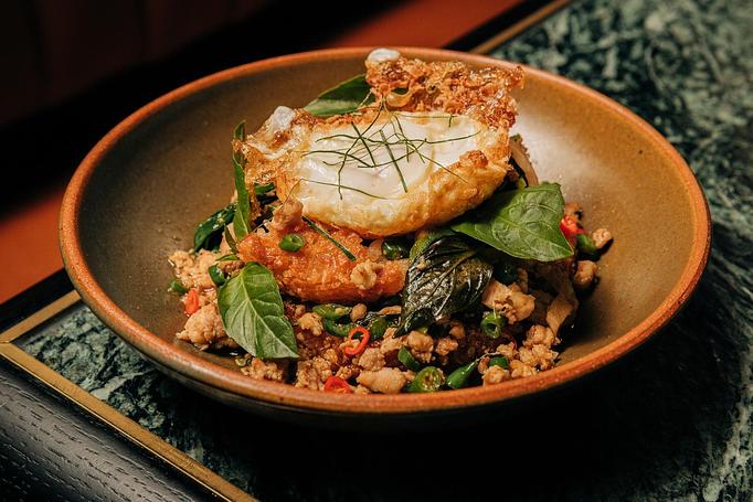 Product: A black bowl filled with a savory dish, including crispy rice, green herbs, and vegetables, topped with a fried egg. - Crying Tiger in Chicago, IL Restaurants/Food & Dining