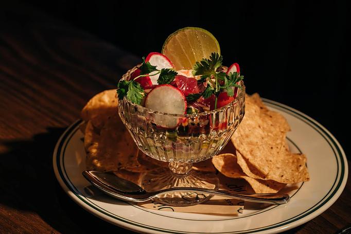 Product: A decorative glass bowl filled with a colorful salad garnished with lime and radish slices sits on a plate surrounded by tortilla chips. - Gus' Sip and Dip in Chicago, IL Restaurants/Food & Dining