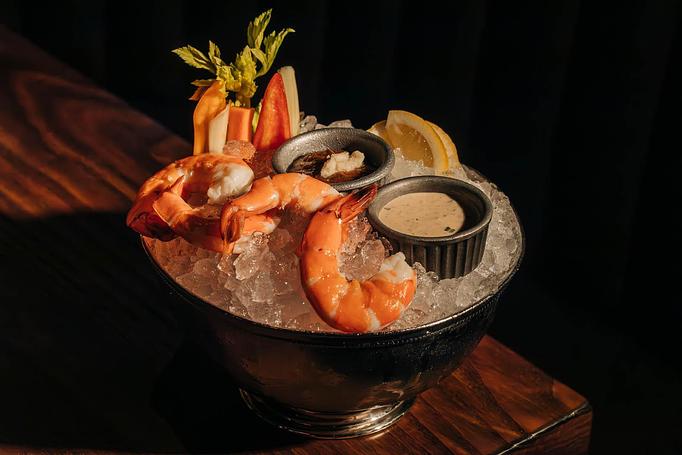 Product: A black bowl filled with ice holds cooked shrimp, lemon wedges, and carrot sticks. Two small dishes with sauce are also placed on top. The setting has a dark background. - Gus' Sip and Dip in Chicago, IL Restaurants/Food & Dining