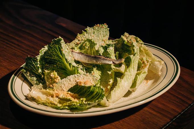 Product: A plate of Caesar salad with romaine lettuce, Caesar dressing, and a single anchovy on top, set on a wooden surface. - Gus' Sip and Dip in Chicago, IL Restaurants/Food & Dining