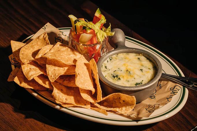 Product: A plate of tortilla chips, a bowl of spinach and artichoke dip, and a small cup of salsa, presented on a wooden table. - Gus' Sip and Dip in Chicago, IL Restaurants/Food & Dining