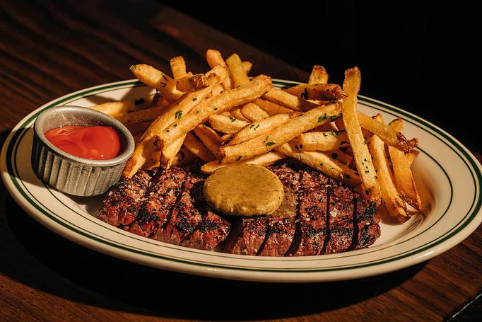 Product: A plate of steak topped with a dollop of sauce, accompanied by a generous serving of thin, seasoned fries. A small dish of ketchup is placed on the side. - Gus' Sip and Dip in Chicago, IL Restaurants/Food & Dining