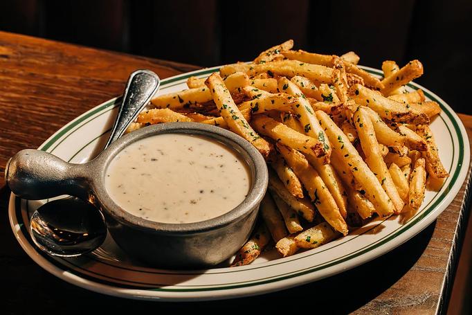 Product: A plate of seasoned French fries accompanied by a small bowl of dipping sauce. - Gus' Sip and Dip in Chicago, IL Restaurants/Food & Dining