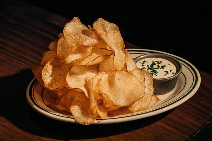 Product: A plate of golden potato chips accompanied by a small dish of creamy dipping sauce garnished with chopped chives. - Gus' Sip and Dip in Chicago, IL Restaurants/Food & Dining