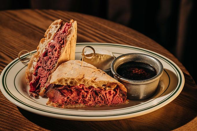 Product: A sandwich filled with sliced wagyu is served on a plate with a side of mustard and a small cup of au jus. - Gus' Sip and Dip in Chicago, IL Restaurants/Food & Dining