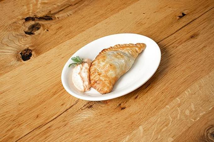 Product: A golden empanada with white sauce and green garnish on an oval white plate on a wooden surface - Cafe Ba-Ba-Reeba! in Lincoln Park - Chicago, IL Gluten Free Restaurants