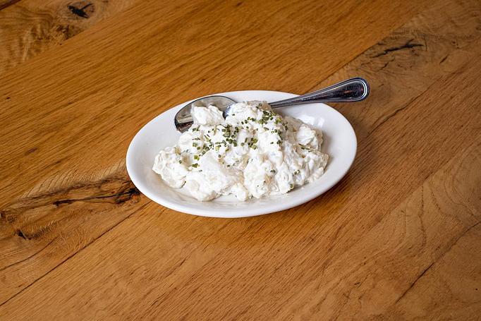 Product: White potato chunks in a mayonnaise sauce topped with green herbs in a white oval dish, on a wooden table - Cafe Ba-Ba-Reeba! in Lincoln Park - Chicago, IL Gluten Free Restaurants