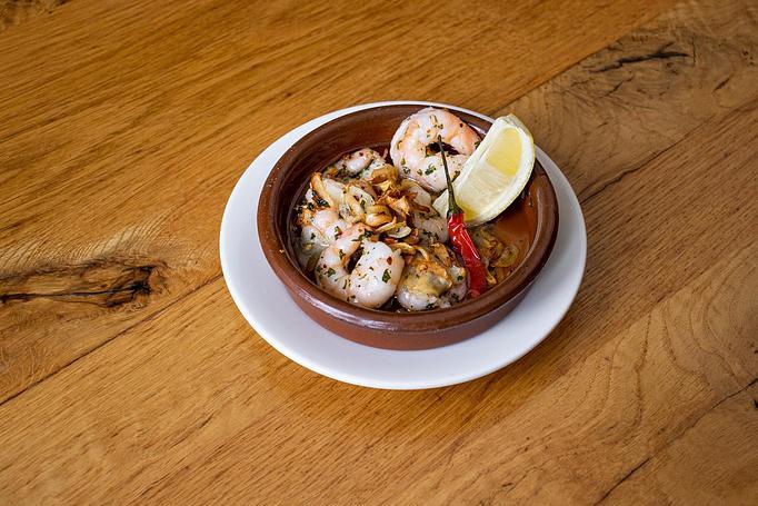 Product: White shrimp with a red pepper and a lemon wedge in a round brown dish on a white dish, sitting on a wooden surface - Cafe Ba-Ba-Reeba! in Lincoln Park - Chicago, IL Gluten Free Restaurants