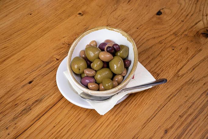 Product: Green and purple olives in a small white dish with a spoon on a wooden table - Cafe Ba-Ba-Reeba! in Lincoln Park - Chicago, IL Gluten Free Restaurants