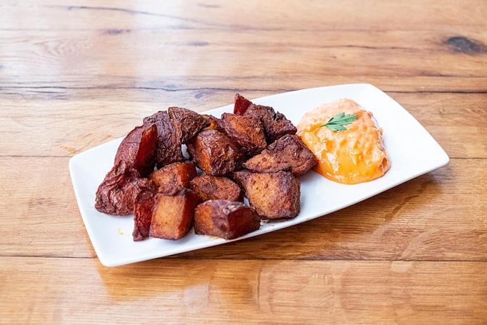 Product: Brown fried potato chunks served with an orange sauce on a rectangular white plate served on a wooden table - Cafe Ba-Ba-Reeba! in Lincoln Park - Chicago, IL Gluten Free Restaurants