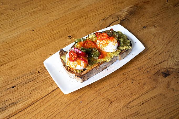Product: A crusty piece of bread topped with green avocado, two poached eggs, red peppers, and orange spices, on a white rectangular plate on a wooden table - Cafe Ba-Ba-Reeba! in Lincoln Park - Chicago, IL Gluten Free Restaurants