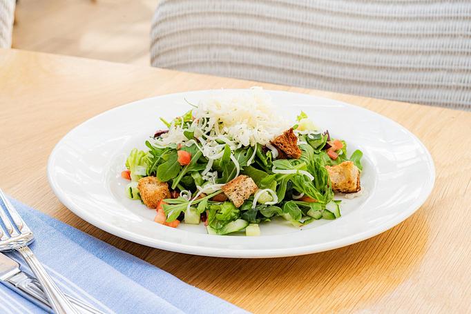 Product: A mixed green salad with cucumber, diced vegetables, croutons, and shredded cheese is served in a white bowl on a wooden table. - Summer House - Las Vegas in Las Vegas, NV Restaurants/Food & Dining