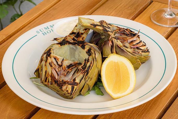 Product: Two grilled artichoke halves with char marks with a lemon on the side. Served on a white plate. - Summer House - Las Vegas in Las Vegas, NV Restaurants/Food & Dining