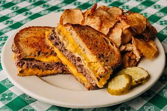 Product: Patty melt and homemade chips served on a white plate with pickle spheres all on a green checkered tablecloth. - RJ Grunts in Lincoln Park - Chicago, IL American Restaurants