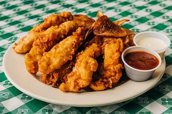 Product: A white plate with crispy chicken tenders, served with a small cup of ranch dressing and a side of ketchup - RJ Grunts in Lincoln Park - Chicago, IL American Restaurants