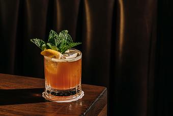 Product: A glass of iced cocktail garnished with mint leaves and a lemon slice, placed on a wooden surface against a dark background. - Gus' Sip and Dip in Chicago, IL Restaurants/Food & Dining