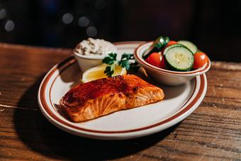 Product: Salmon fillet glazed with barbecue sauce served on a plate with a lemon wedge, sauce in a ramekin and bowl of cucumber-tomato salad - Bub City in Rosemont, IL Barbecue Restaurants