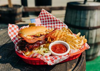 Product: Sandwich topped with bacon served in a red basket on top of red checkered tissue paper with waffle-style French fries and a ramekin of ketchup - Bub City in Rosemont, IL Barbecue Restaurants