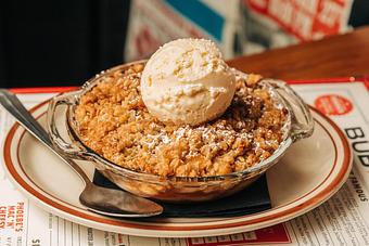 Product: Clear glass bowl filled with a crumbly apple dessert and topped with a scoop of vanilla ice cream - Bub City in Rosemont, IL Barbecue Restaurants
