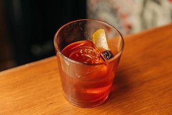 Product: Rocks-style cocktail glass filled with light brown beverage, ice, cherry and orange peel slice - Bub City in Rosemont, IL Barbecue Restaurants