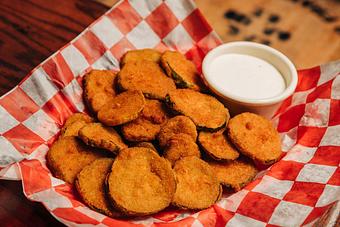Product: A pile of crunchy fried pickle slices served with a ramekin of ranch dressing on top of red checkered tissue paper - Bub City in Rosemont, IL Barbecue Restaurants