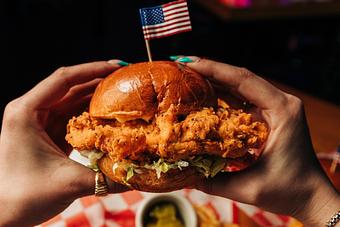 Product: Two hands holding a crispy fried chicken sandwich with an American flag toothpick stuck through the center - Bub City in Rosemont, IL Barbecue Restaurants