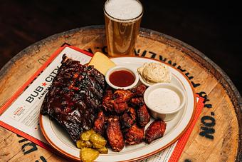 Product: White plate containing a half-slab of baby back ribs and smoked, sauceless chicken wings with pickles, a slice of toast and ramekins of sauces and coleslaw - Bub City in Rosemont, IL Barbecue Restaurants