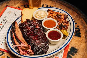 Product: Large white plate containing a half-slab of saucy baby back ribs, slices of brisket meat, a slice of toast, pulled pork meat and pickled veggies with ramekins of sauces and coleslaw - Bub City in Rosemont, IL Barbecue Restaurants