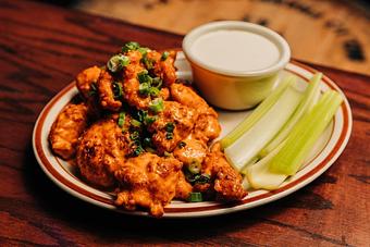 Product: A pile of chicken nuggets tossed in buffalo sauce served on a white plate with celery slices and a ramekin of blue cheese dressing - Bub City in Rosemont, IL Barbecue Restaurants