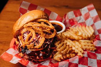 Product: Pulled pork sandwich topped with crispy fried onion slices and served with waffle-style fries and a ramekin of barbecue sauce - Bub City in Rosemont, IL Barbecue Restaurants