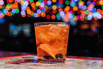 Product: Rock cocktail glass containing a light brown beverage with an orange peel slice and cherries at the bottom of the glass - Bub City in Rosemont, IL Barbecue Restaurants