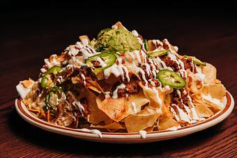 Product: Large pile of tortilla chips on a white plate topped with chicken, guacamole, salsa, jalapeno slices, cheese and sour cream drizzles - Bub City in Rosemont, IL Barbecue Restaurants