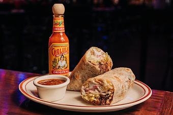 Product: Burrito sliced in half served on a white plate with a side of salsa in a ramekin and a bottle of hot sauce in the background - Bub City in Rosemont, IL Barbecue Restaurants