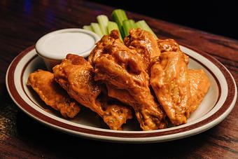 Product: Six wings tossed in buffalo sauce stacked on a plate with celery slices and a ramekin of blue cheese dressing - Bub City in Rosemont, IL Barbecue Restaurants