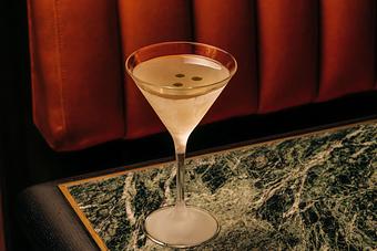 Product: A martini glass filled with a clear cocktail, set on a marble table. The background features a plush, red upholstered surface. - Crying Tiger in Chicago, IL Restaurants/Food & Dining