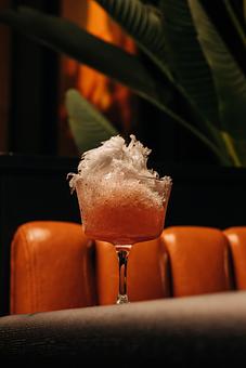 Product: A cocktail glass filled with a pinkish drink topped with shaved ice. The background features orange cushions and green foliage. - Crying Tiger in Chicago, IL Restaurants/Food & Dining