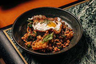 Product: A black bowl filled with a savory dish, including crispy rice, green herbs, and vegetables, topped with a fried egg. - Crying Tiger in Chicago, IL Restaurants/Food & Dining