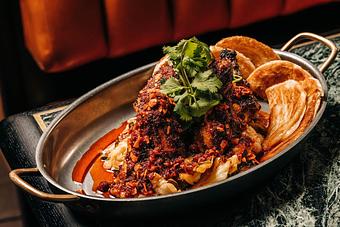 Product: A dish of barbecue chicken topped with spicy red sauce and garnished with fresh cilantro, served in a metal pan. In the background, there is a blurred red cushioned seat. - Crying Tiger in Chicago, IL Restaurants/Food & Dining