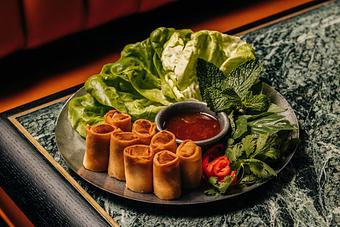 Product: A plate of neatly arranged spring rolls with a small bowl of dipping sauce, surrounded by fresh lettuce, mint leaves, and sliced chili peppers. - Crying Tiger in Chicago, IL Restaurants/Food & Dining