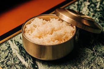 Product: A brass container filled with cooked white rice, partially covered with a lid, placed on a decorative surface. - Crying Tiger in Chicago, IL Restaurants/Food & Dining
